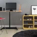 Black single-column standing desk with a monitor and laptop beside yellow shelving