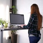 Person standing at a gray desk while using a desktop computer